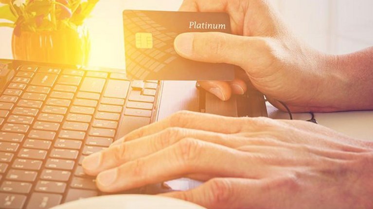 A man has his hands on the keyboard of his laptop and holds a credit card in his hand
