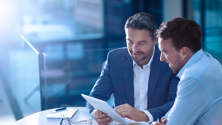 Two business men sitting together holding and discussing what they see on the tablet