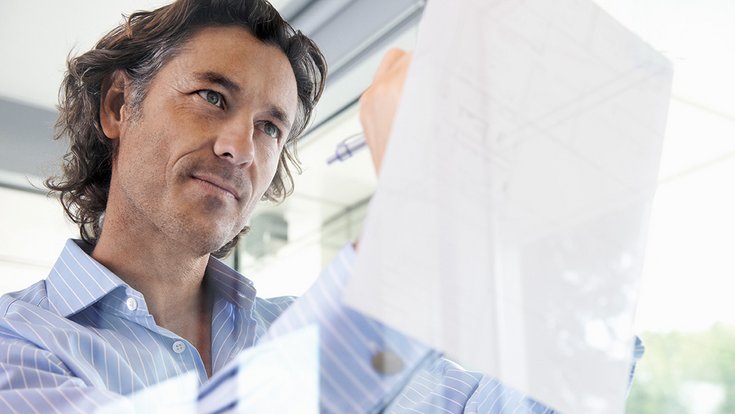 A man with a business shirt notes something on a piece of paper