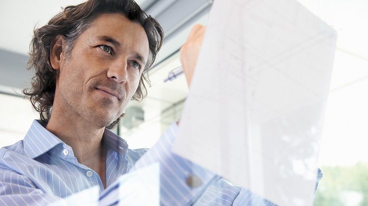 A man with a business shirt notes something on a piece of paper