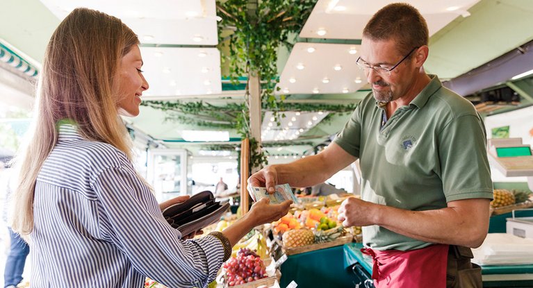 A woman pays with banknotes at a vegetable market stall