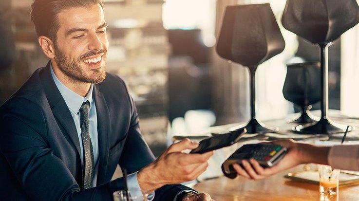 A smiling businessman pays contactless with his smartphone in a restaurant