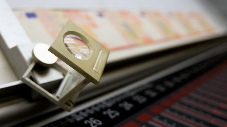 Individual banknotes lie on a device with a magnifying glass
