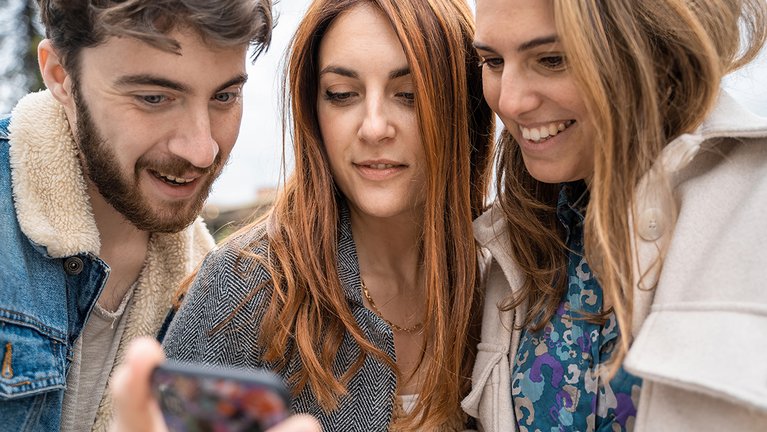 Two young women and a young man look at a certain thing together