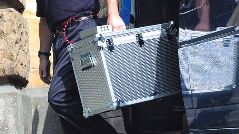 A security guard carries an aluminum suitcase out of a building