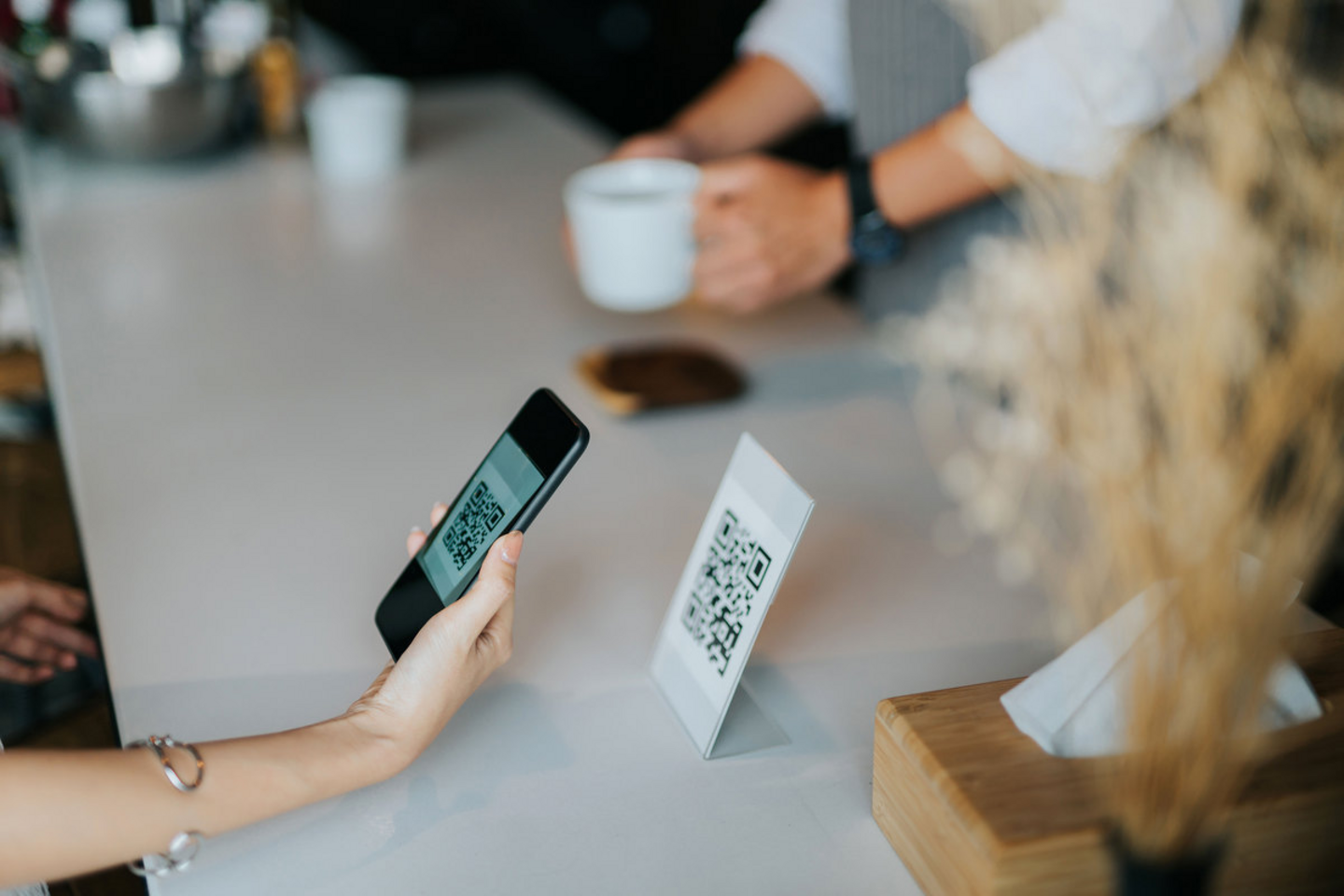 Woman’s hand holding smartphone, scanning barcode for contactless payment in the café during a pandemic.